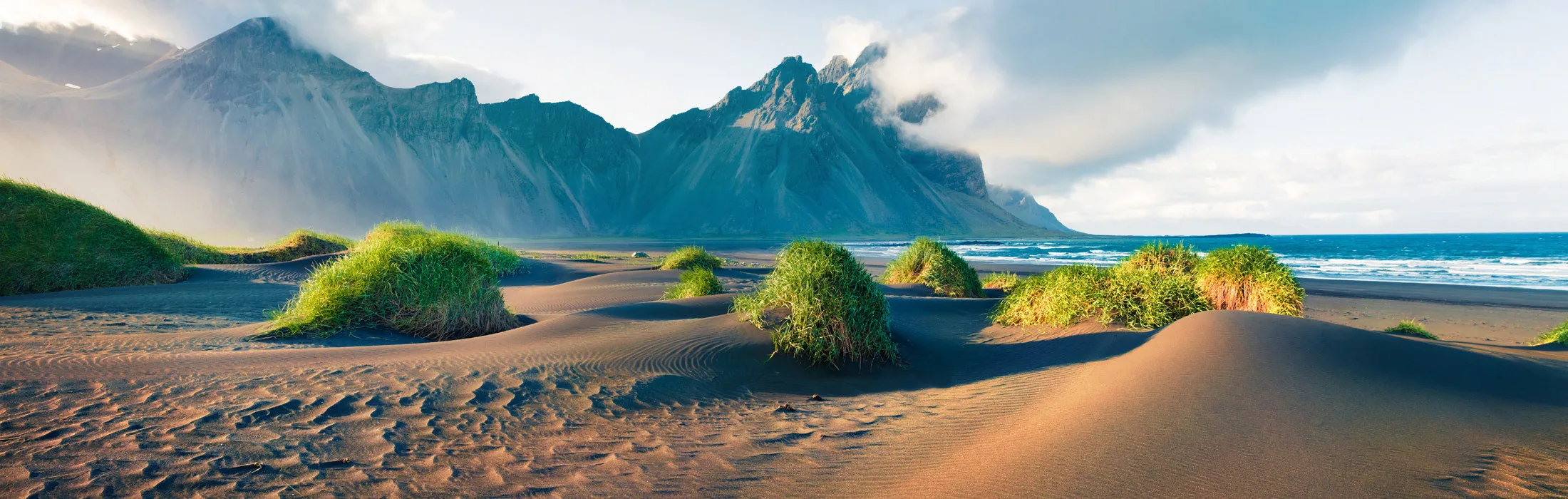 Berge von Stokksnes in Südostisland, davor Grasbüschel im Sandstrand